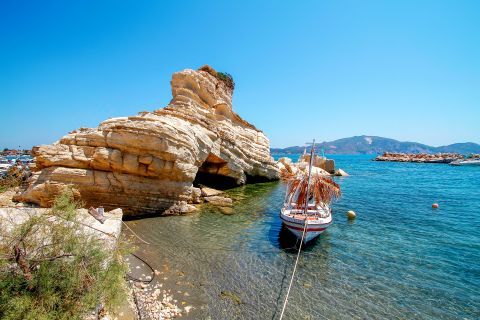 Agios Sostis: A massive rock and a small boat, mooring on crystal clear waters.